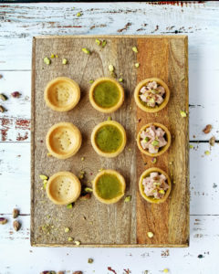 Mortadella and pistachio mini tarts with other incomplete tart shells neatly lined a wooden tray