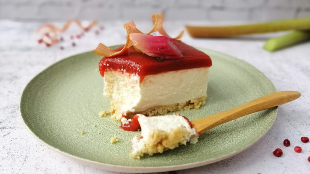A slice of rhubarb and yoghurt tart seen from the side, showing the layers of crumbly base, yoghurt cream and rhubarb puree