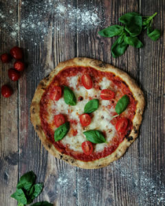 Charred thin crust pizza margherita with fresh cherry tomatoes and basil leaves