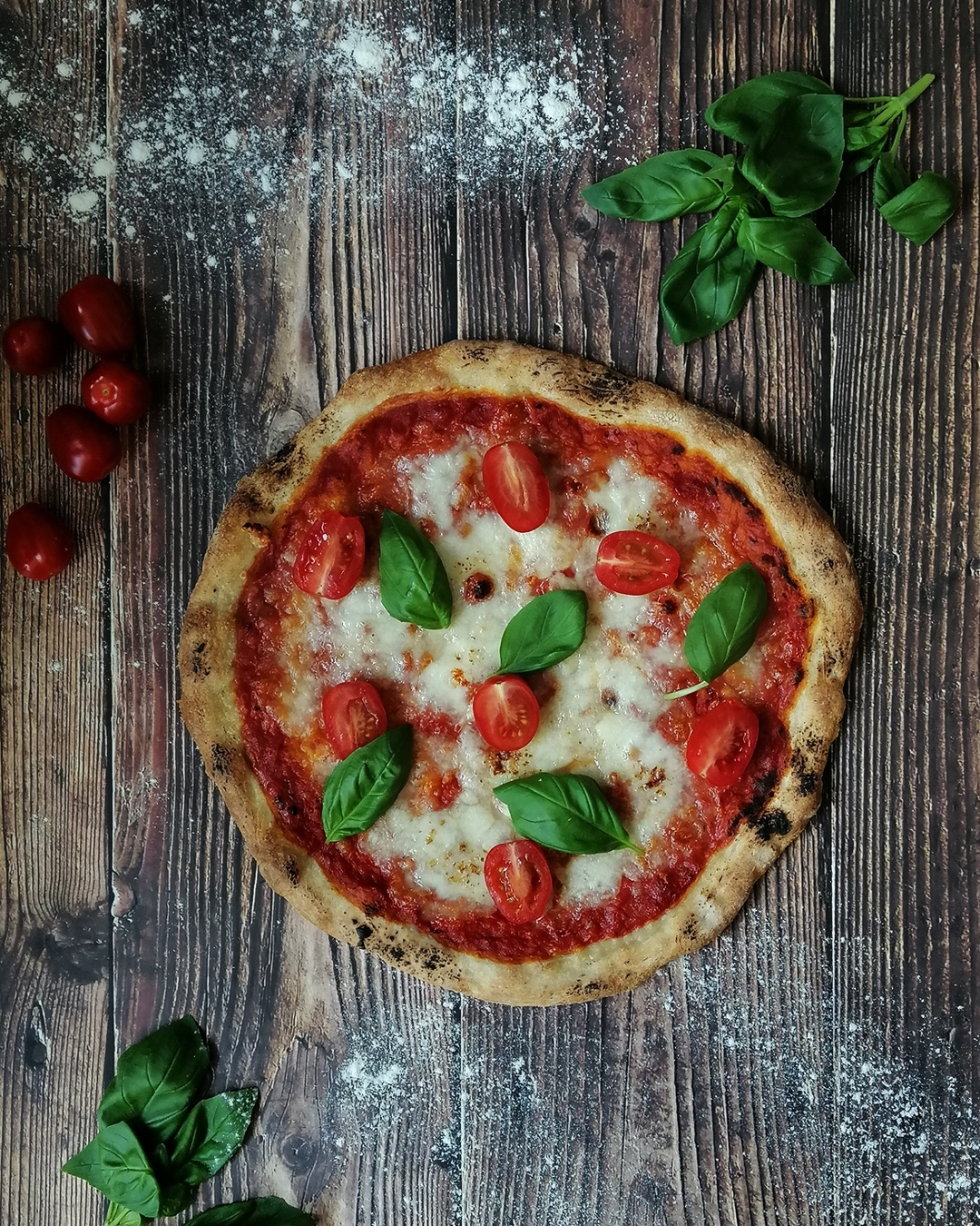 Charred thin crust pizza margherita with fresh cherry tomatoes and basil leaves