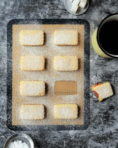 Rhubarb-filled orange biscuits lined on a baking mat, surrounded by a cup of tea, half eaten biscuit