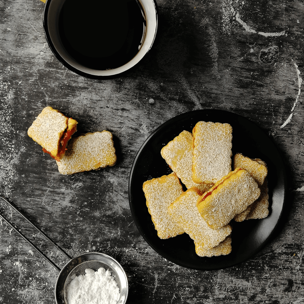 Rhubarb-filled orange biscuits piled on a plate, with a half eaten biscuit and cup of black tea