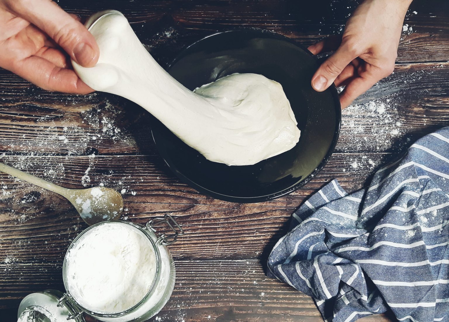 Hands stretching pizza dough from a bowl