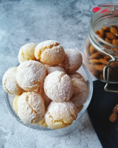 Soft amaretti biscuits in a glass, dusted with icing sugar and a jar of almonds in the background. Copyright: the italian baker