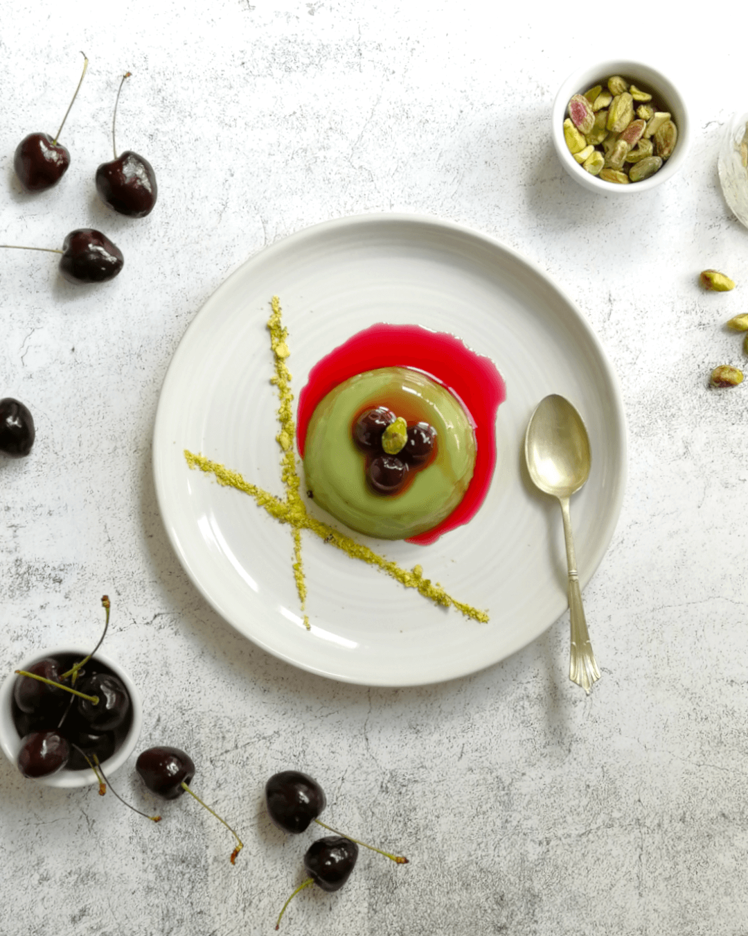 Pistacchio panna cotta seen from overhead, topped with three amarena cherries and purple cherry syrup