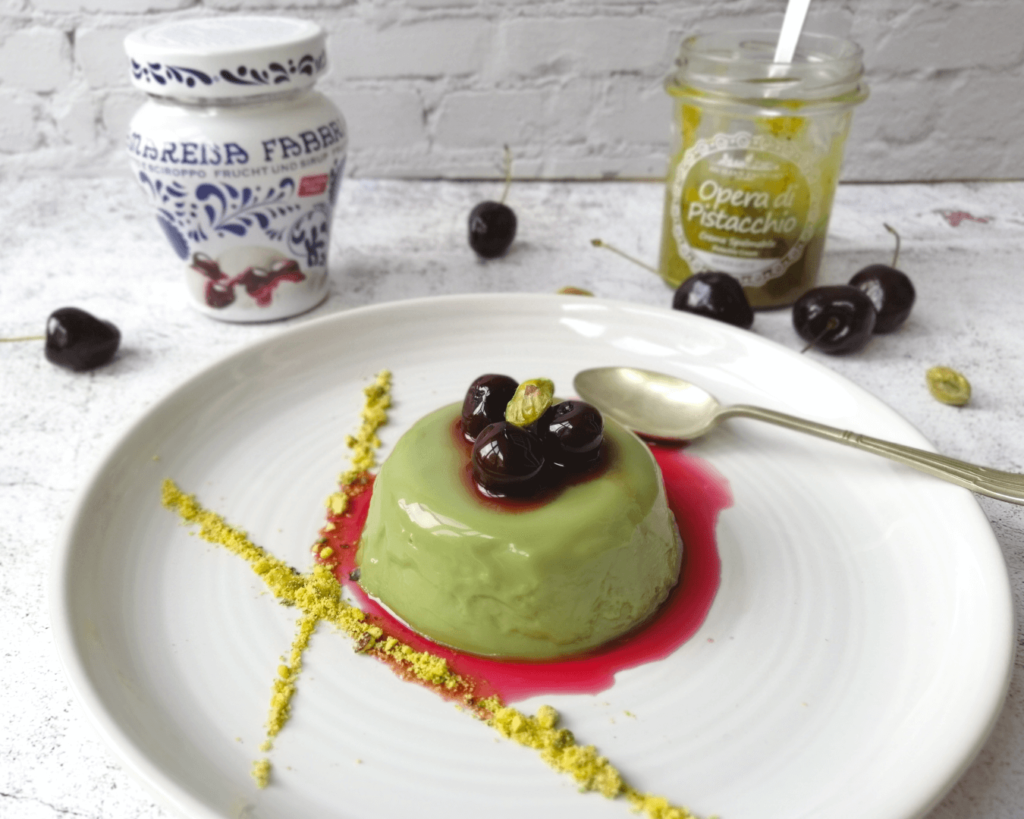 Pistacchio panna cotta topped by three amarena sour cherries, cherry syrup and lines of pistachio powder